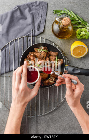 7/8-Ansicht von Frau hinzufügen souce in gebratenes Fleisch mit Öl, Brokkoli und Zitrone Stockfoto