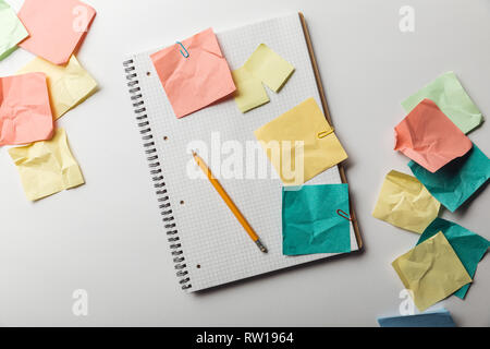 Blick von oben auf die Notebook mit leeren squared Seite in der Nähe von Zerknitterten bunte Haftnotizen auf weißem Hintergrund Stockfoto