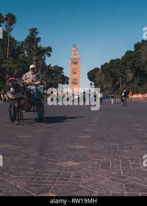 Marrakesch, Marokko - 27. März 2018: die Straßen von Marrakesch mit Koutoubia Moschee im Hintergrund. Schlitten-, Roller- und Menschen auf den Straßen, blauer Himmel. Stockfoto