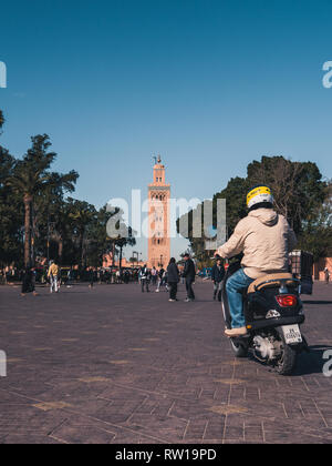 Marrakesch, Marokko - 27. März 2018: die Straßen von Marrakesch mit Koutoubia Moschee im Hintergrund. Schlitten-, Roller- und Menschen auf den Straßen, blauer Himmel. Stockfoto