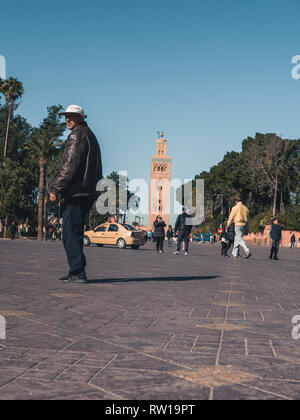 Marrakesch, Marokko - 27. März 2018: die Straßen von Marrakesch mit Koutoubia Moschee im Hintergrund. Schlitten-, Roller- und Menschen auf den Straßen, blauer Himmel. Stockfoto