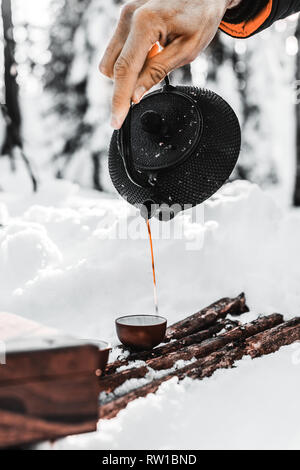 Teilansicht der männlichen Reisenden gießen Tee aus Wasserkocher in Schale im Winter Wald Stockfoto