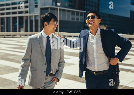Zwei lächelnde asiatische Geschäftsleute sprechen und zu Fuß in die Stadt. Business Partner zusammen gehen im Freien. Stockfoto