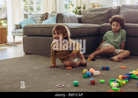 Zwei Kinder sitzen auf dem Boden mit ihrem Spielzeug und Spielen. Kinder spielen zu Hause mit Bausteinen. Stockfoto
