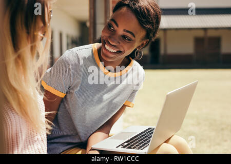 Lächelnd weibliche Studenten am College Campus mit Laptop sitzen. Zwei junge Studenten an der High School Campus mit Laptop sitzen. Stockfoto