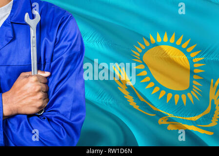 Kasachischen Mechaniker in der blauen Uniform hält Schraubenschlüssel gegen Kasachstan Flagge schwenkten Hintergrund. Gekreuzte Arme Techniker. Stockfoto