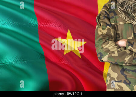 Gekreuzte Arme kamerunischen Soldaten mit nationalen wehende Flagge auf Hintergrund - Kamerun militärischen Thema. Stockfoto