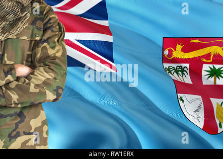 Gekreuzte Arme Fijian Soldat mit nationalen wehende Flagge auf Hintergrund - Fidschi militärischen Thema. Stockfoto