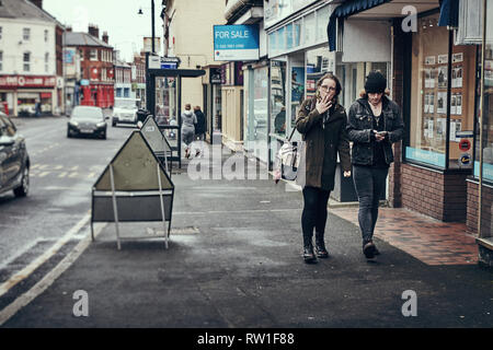 Harwich & Dovercourt, Essex, England - 3. März 2019: eine Frau mit einer Zigarette und einen Mann auf seinem Telefon zu Fuß durch Harwich High Street. Stockfoto