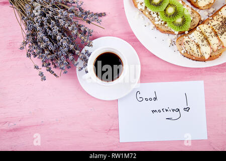 Kaffeebecher und gesundes Frühstück mit Toast blumenstrauß Lavendel und Notizen guten Morgen auf rosa Tabelle. schönen Frühstück, Grußkarte, zu Stockfoto