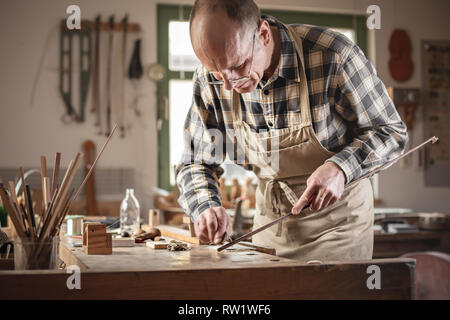 Ausgereifte handwerkliche Arbeiten an einem geigenbogen in einem Workshop Stockfoto