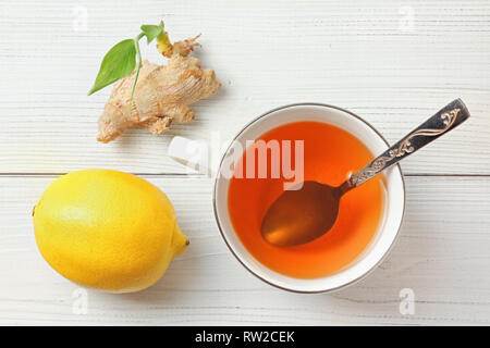 Weißes Porzellan Schale, silbernen Löffel, Hot orange Tee, Zitrone und Ingwer Wurzel mit Grün sprießen. Ansicht von oben, holzbretter unter. Stockfoto