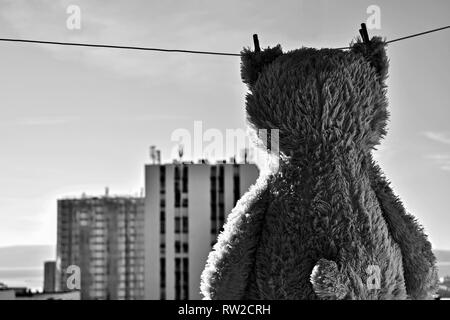 Teddybär Spielzeug am Seil hängend von wäscheklammer mit Gebäude im Hintergrund/Stadtblick - Bild Stockfoto