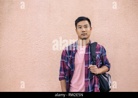 Selbstbewussten jungen asiatischen Mann stand draußen mit einem Rucksack Stockfoto