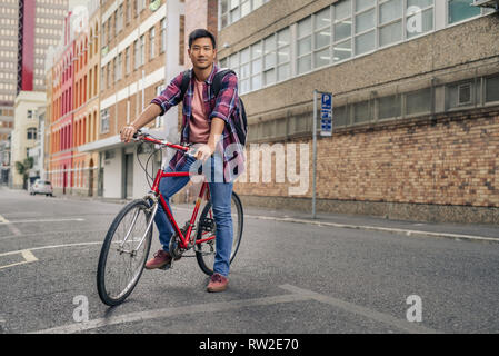 Lächelnden jungen Mann sitzt auf seinem Fahrrad in der Stadt Stockfoto