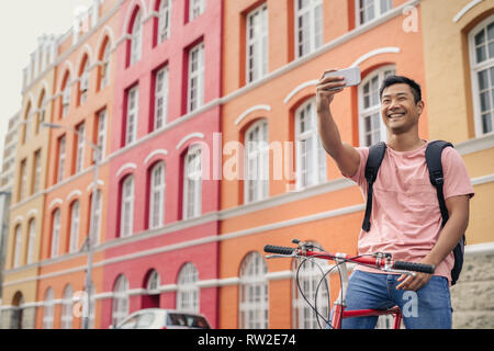Lächelnden jungen Mann sitzt auf seinem Fahrrad eine selfie Stockfoto