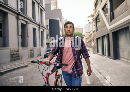 Jungen asiatischen Mann mit seinem Fahrrad durch die Straßen der Stadt Stockfoto