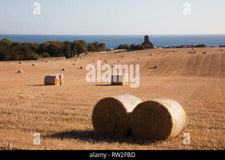 Blick über den goldenen Feld von runden Strohballen zu Dorf Kirche an der Ostküste. St Abbs, Berwickshire, Scottish Borders, Schottland, Großbritannien, Großbritannien Stockfoto