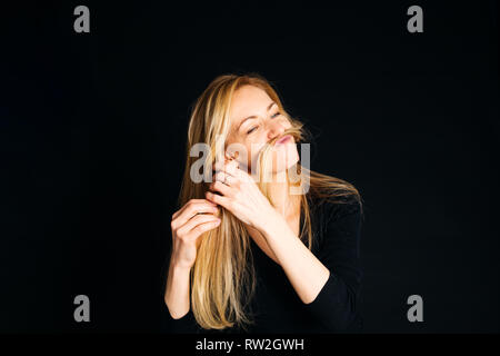 Nahaufnahme, Porträt einer Frau mit einem dummen Moment, während gegen den schwarzen Hintergrund posiert im Studio Stockfoto