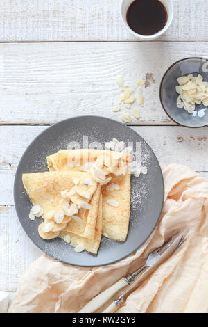 Crepes mit Bananen und Mandelblättchen und Kaffee auf einem weißen Tisch Stockfoto