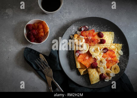 Crepes mit Bananen, Blut Orangenscheiben und Himbeeren auf einem dunklen Hintergrund Stockfoto