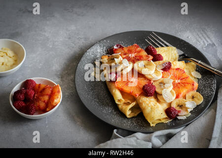 Crepes mit Bananen, Blut Orangenscheiben und Himbeeren auf einem dunklen Hintergrund Stockfoto