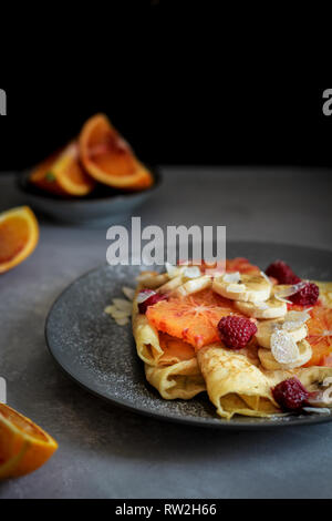 Crepes mit Bananen, Blut Orangenscheiben und Himbeeren auf einem dunklen Hintergrund Stockfoto
