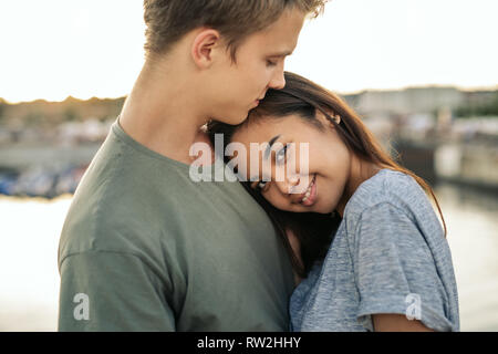 Lächelnde junge Frau ihrem Freund außerhalb Umarmen von Hafen Stockfoto