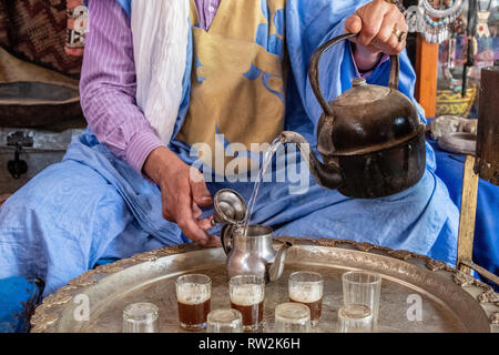 Berber Mann mit Turban und deraa gießt Tee von Teekanne in Gläser für traditionellen marokkanischen Teezeremonie, Tighmert Oase, Marokko Stockfoto