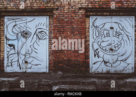 Street Art auf zwei weiße Türen aus rotem Backstein Gebäude in Riga. Stockfoto