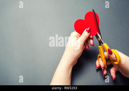 Mädchen schneidet die roten Herzen mit einer Schere. Das Konzept der Abbruch der Beziehungen, Streit und Scheidung. Verrat an den Anderen. Verlust der Gefühle für deine Liebe Stockfoto