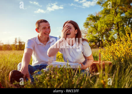 Glücklich lachend ein Paar essen Pizza außerhalb. Frau und Mann in Picknick bei Sonnenuntergang. Kerle heraus zusammen hängen und Spaß haben. Stockfoto