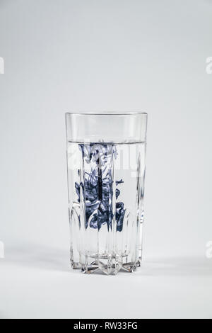 Wasserverschmutzung Konzept. Dunkle Substanz verschmutzt reinigen Wasser in einem Glas mit weißem Hintergrund Stockfoto
