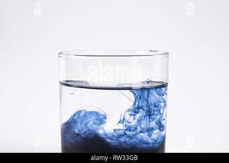 Verunreinigung mit Wasser Konzept. Dunkle Substanz auflösen mit sauberem Wasser in ein Glas mit weißem Hintergrund, Nahaufnahme Stockfoto