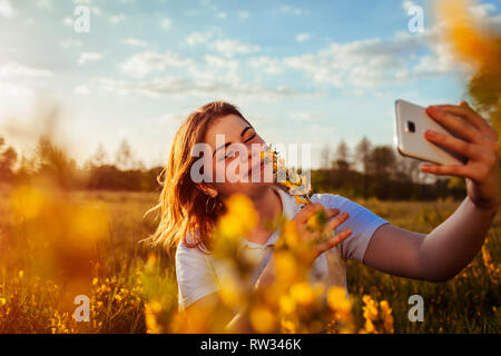 Junge Frau von selfie im Frühjahr blühenden Feld bei Sonnenuntergang. Allergiefrei. Glücklich lächelnde Mädchen entspannt und genießt die Natur. Stockfoto