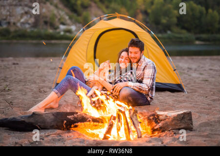 Leute, Sommer Tourismus und Natur Konzept - Paar in der Nähe von Camp Feuer Aufwärmen aus dem Zelt gesehen Stockfoto