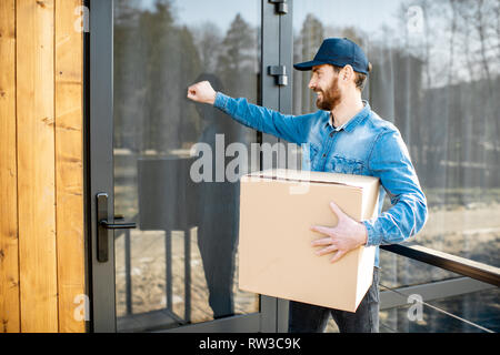 Delivery Man klopft Tür Der moderne Haus, liefern einige Güter in der Papier-Paket home Stockfoto