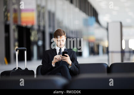 Portrait der junge Unternehmer mit Smartphone sitzen auf Leder Stuhl im Flughafen, kopieren Raum Stockfoto