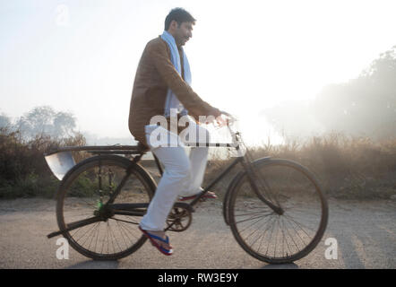 Bauer oder Dorf Mann auf einem Fahrrad mit einem Spaten auf dem Wagen des Fahrrades. Stockfoto