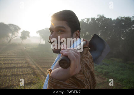 Seitenansicht eines lächelnden Landwirt in seiner Landwirtschaft Feld mit einem Spaten auf seine Schultern mit Sonne in den Hintergrund. Stockfoto