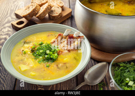 Duftende gelbe Erbsen Suppe mit geräuchertem Rippchen auf einem Holztisch. Stockfoto