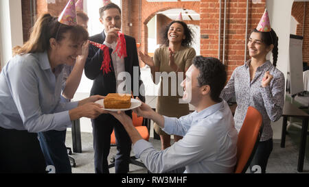 Freundlich diverse Mitarbeiter in parteihüte präsentiert Kuchen gratulieren Kollegen Stockfoto