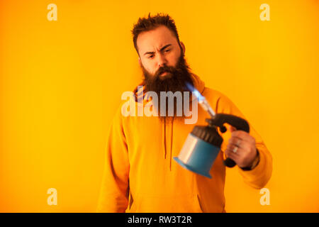 Bärtige handy man Holding Brenner auf gelben Hintergrund. Professionelles Werkzeug. Blue Tool Stockfoto