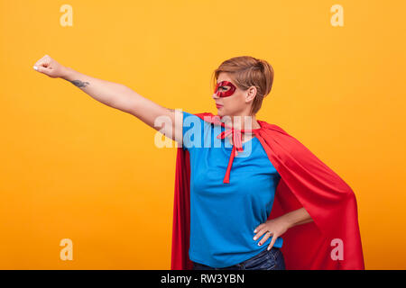 Junge Frau dresed wie Superheldinnen Fliegen in der ganzen Welt gelben Hintergrund zu speichern. Frau Superkräfte. Stockfoto