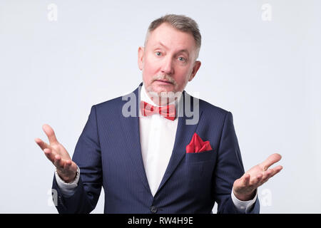 Freundlich älterer Mann im blauen Anzug duscussing Frage mit ihnen mit offenen Händen Geste und lächelte Kamera Stockfoto