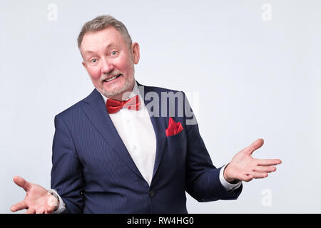 Freundlich älterer Mann im blauen Anzug duscussing Frage mit ihnen mit offenen Händen Geste und lächelte Kamera Stockfoto