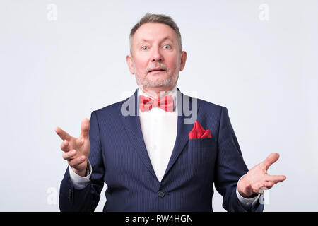 Freundlich älterer Mann im blauen Anzug duscussing Frage mit ihnen mit offenen Händen Geste und lächelte Kamera Stockfoto