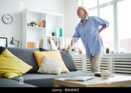 Portrait des modernen ältere Frau mit Rückenbeschwerden lehnte sich auf dem Sofa Platz, kopieren Stockfoto