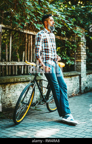 Ein hübscher junger Mann geht in die Stadt fahren mit dem Fahrrad, daneben zu stehen und zu überlegen, wo er gehen würde. Stockfoto