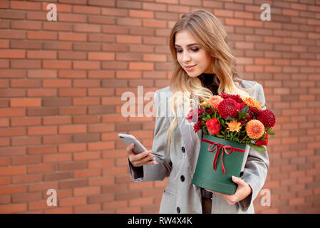 Schöne Mädchen schaut in das Telefon in der Hand halten sie ein grünes Feld mit hellen Farben Stockfoto